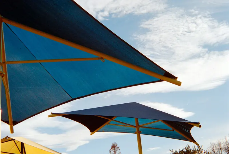 Blue fabric shade canopies on steel posts against a cloudy sky