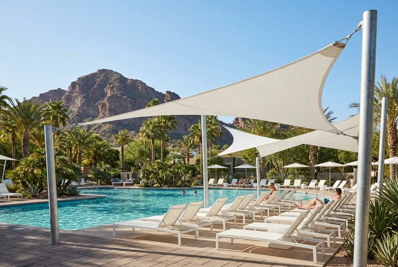 White triangle shade sails over a Scottsdale resort pool with lounge chairs and Camelback Mountain behind